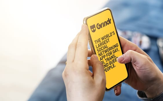 San Francisco, CA, US, May 2022: Woman holding a phone with Grindr mobile application on screen. In background the Grindr logo blurred. Grindr is dating application for gay, bi, trans, and queer people