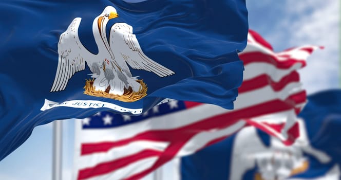 The Louisiana state flag waving along with the national flag of the United States of America. In the background there is a clear sky. Louisiana is a state in the Deep South regions of the US