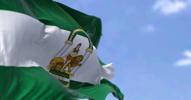 Andalusian flag waving in the wind on a clear day. Andalusia is the southernmost autonomous community in Peninsular Spain, the most populous and the second largest autonomous community in the country