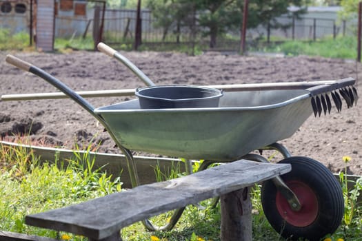 Gray metal garden wheelbarrow with two handles and one wheel. The wheelbarrow is in the garden or garden. Gardener's wheelbarrow in the backyard. Garden cleaning