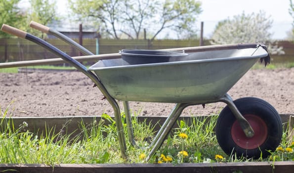 Gray metal garden wheelbarrow with two handles and one wheel. The wheelbarrow is in the garden or garden. Gardener's wheelbarrow in the backyard. Garden cleaning