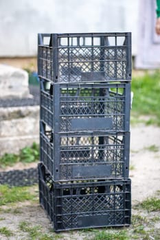 Plastic empty black boxes stacked together for plants or harvest. On a sunny day in early spring. Gardening concept. Household crop collection and storage boxes standing in the backyard