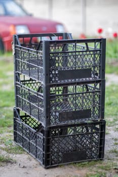 Plastic empty black boxes stacked together for plants or harvest. On a sunny day in early spring. Gardening concept. Household crop collection and storage boxes standing in the backyard