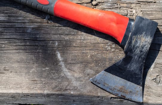 A sharp ax with an ergonomic rubberized handle on a wooden background. The ax is intended for rough, rough processing of wood. Has a forged heat treated carbon steel wedge