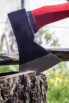 An ax with a red handle plunges into a stump. Sawmill operation concept. Woodworking. Stump and ax in sunny weather. Preparing firewood for the winter. Selective focus, blurred background