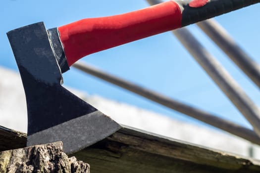 A new modern ax with a red handle sticks out of a wooden stump against a green meadow on a summer sunny day. The ax stuck into the stump. Ax blade in a log
