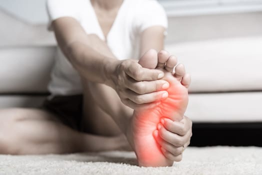 Foot pain, Asian woman feeling pain in her foot at home, female suffering from feet ache use hand massage relax muscle from soles in home interior, Healthcare problems and podiatry medical concept