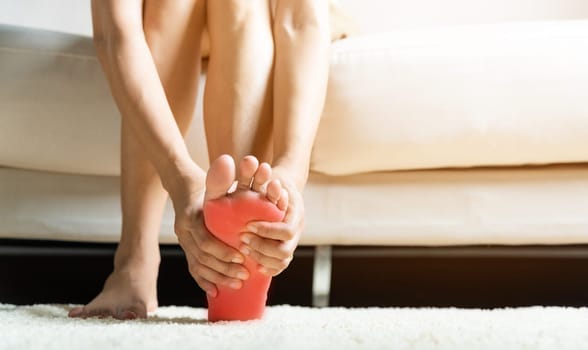 Foot pain, Asian woman sitting on sofa feeling pain in her foot at home, female suffering from feet ache use hand massage relax muscle from soles in home interior, Healthcare and podiatry medical