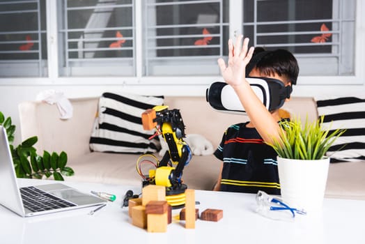 Virtual Reality Simulator. Asian kid boy using VR glasses on robotic arm in workshop, Child learning programer control robot arm with sensors to pick up wood block, Technology education. industry 4.0