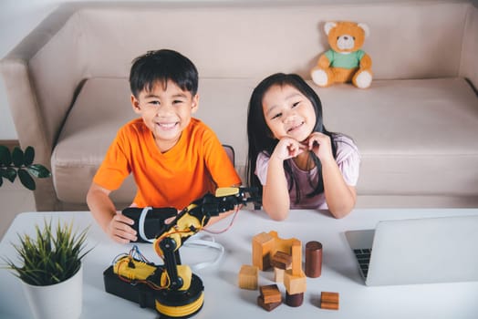 Two children programming and testing robot arm their science, Kid little girl program code to robot with laptop computer and the boy test with remote control to pick up wood block, education lesson