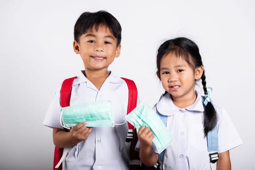 Two Asian student kid girl boy brother sister wearing student thai uniform holding protect mask ready to go to school in studio shot isolated on white background, new normal back to school