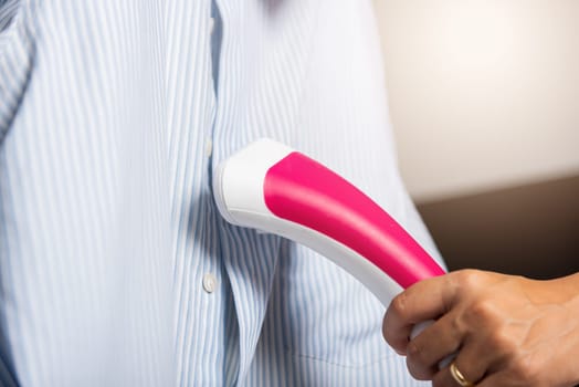 Close up of woman using electric hand steam generator while it is hot and steam comes out for clothes shirt at house, Household & home equipment for housework, concept of linen care