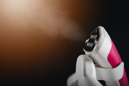 Close up of electric hand steam generator while it's hot and steam comes out on the ironing board place for clothes on black background, Household & home equipment for housework, concept of linen care