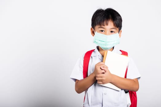 Asian student kid boy wearing student thai uniform and medical protect face mask and hugging note book in studio shot isolated on white background, new normal back to school