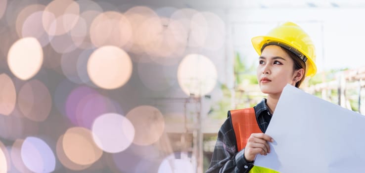 Asian engineer architect worker woman holding blueprint infrastructure progress at construction site, engineering female leader standing hold paper plan control worker to building project