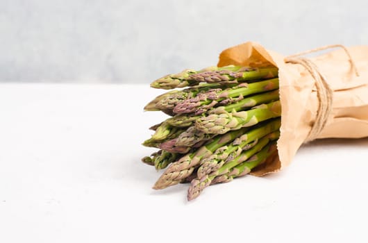 Fresh green bundle of asparagus on a white textured table, vegetables in spring, gourmet cuisine food, cooking a vegan meal