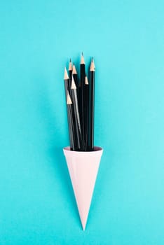 Black pencils in a cone on a blue background, minimalism, creative, surreal and education concept, copy space for text, pastel colored wall