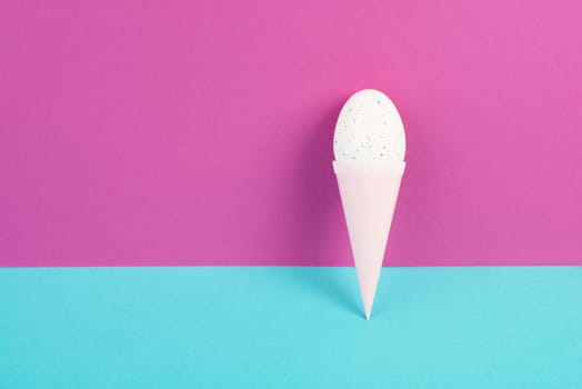 Ice cream cone with an egg, pink and blue background, copy space, easter holiday, summer season, minimalism and creative concept, greeting card