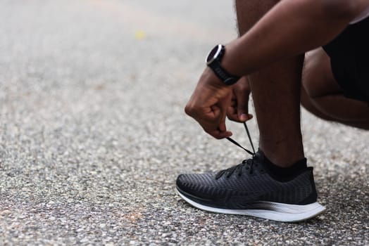 Close up Asian sport runner black man wear watch sitting he trying shoelace running shoes getting ready for jogging and run at the outdoor street health park, healthy exercise workout concept