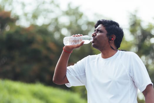 Close up Asian young sport runner black man wear athlete headphones he drinking water from a bottle after running at the outdoor street health park, healthy exercise workout concept