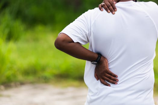 Close up Asian young sport runner black man wear watch hands joint hold back and shoulder he is pain while running at the outdoor street health park, healthy exercise Injury from workout concept