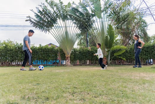 Asian young mother, father and child daughter playing soccer outside in nature a field garden park. Happy family kid funny play football together in summer, sport and exercises for healthy lifestyle