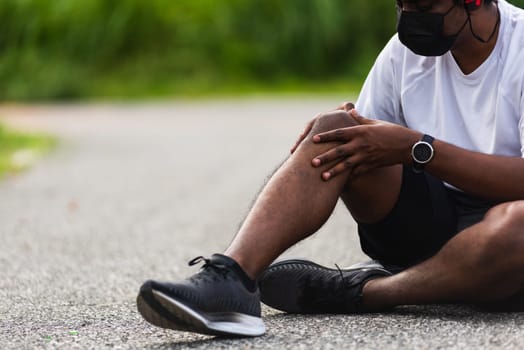 Close up Asian sport runner black man wear watch sitting he uses hands joint hold on his knee while running at the outdoor street health park, healthy exercise Injury from workout concept