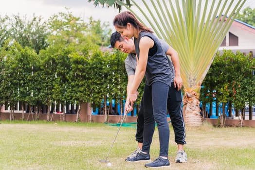 Asian young man support teaching training woman to play perfect golf while standing together in nature a field garden park. Couple trainer giving a lesson on the golf course
