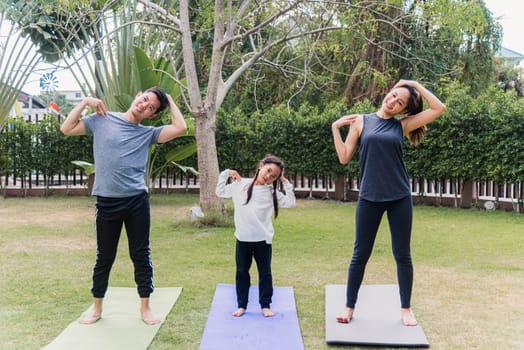 Asian young mother, father and child daughter practicing exercising stretching together before yoga workout outdoor morning in nature a field garden park. Happy family kid sport healthy lifestyle