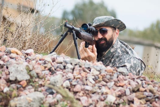 The hunter or military person is hiding and aiming with sniper outdoors.