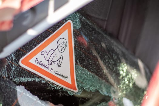 Warning sign of children inside a car after an accident with bloody broken glass. Translation: Child in the car. Close-up of white baby on board sticker on car back window