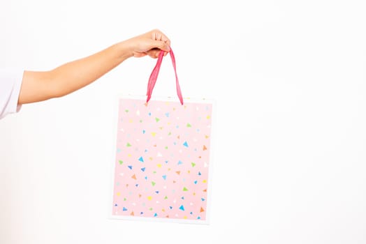 Closeup women hand holding a colorful pink shopping bag, studio shot isolated on white background, female holds in hand white clear empty blank craft paper gift bag for purchases