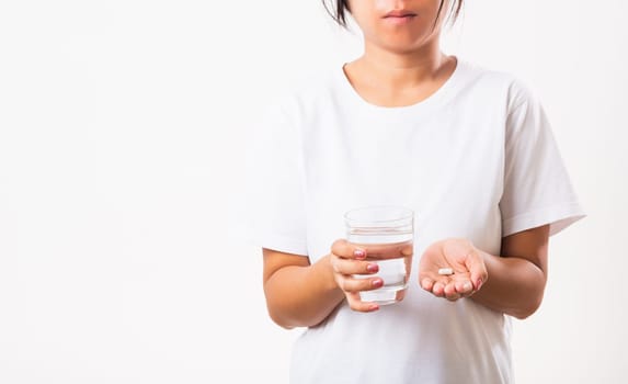 Closeup young Asian woman hold pill drugs in hand ready take medicines with a glass of water, studio shot isolated on white background, Healthcare and medical pharmacy concept