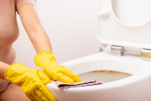 Hands of Asian woman cleaning toilet seat by pink cloth wipe restroom at house, female wearing yellow rubber gloves she sitting and cleanup or washing bathroom, Housekeeper healthcare concept