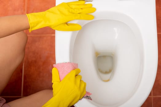 Hands of Asian woman cleaning toilet seat by pink cloth wipe restroom at house, female wearing yellow rubber gloves she sitting and cleanup or washing bathroom, Housekeeper healthcare concept