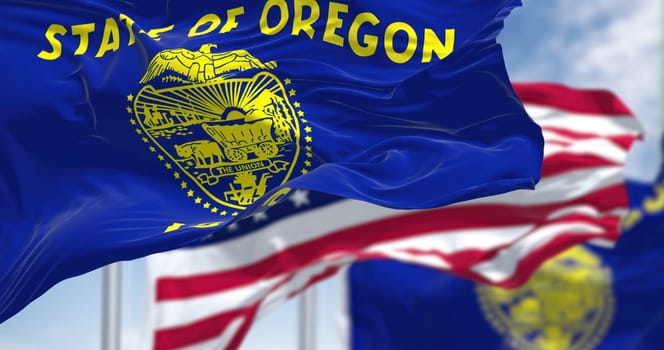 The Oregon state flag waving along with the national flag of the United States of America. In the background there is a clear sky. Oregon is a U.S. state in the northwest