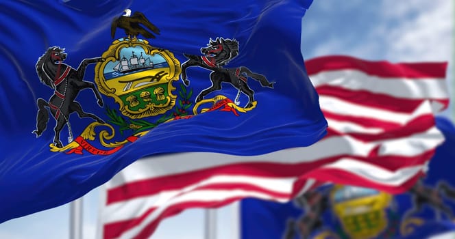The Pennsylvania state flag waving along with the national flag of the United States of America. In the background there is a clear sky. Pennsylvania is a U.S. state in the northeast