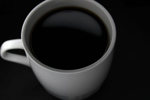 White mug with black coffee on a black background. View from above. Close-up..