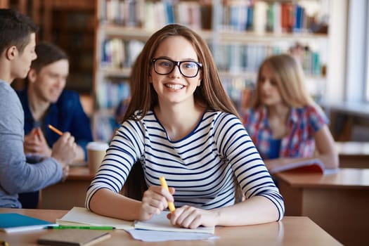 Pretty teenage girl in casualwear looking at camera by desk