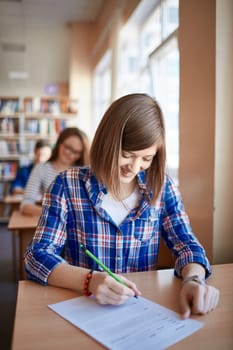 Happy girl filling in gaps in test form at lesson in college