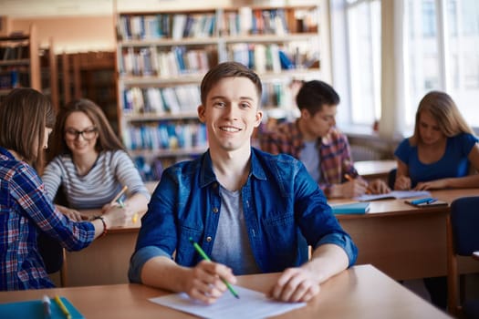 Teenage guy in casualwear looking at camera by desk