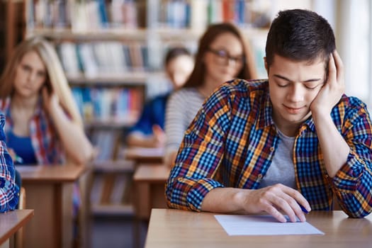Pensive guy carrying out test on background of his classmates