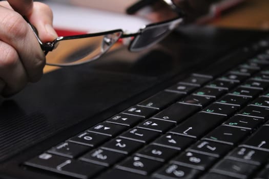A girl sitting at a laptop holds glasses in her hands. Business concept. Work from home..