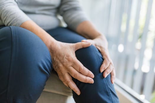 Senior woman sitting on bench, holding her painful knee