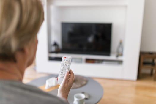Senior woman with remote control watching television