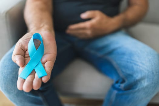 Senior man holding a blue cancer awareness ribbon in hand