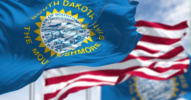 The South Dakota state flag waving along with the national flag of the United States of America. South Dakota is a U.S. state in the North Central region of the United States