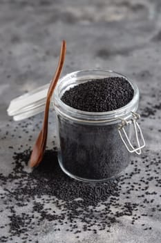 Indian spice Black cumin (nigella sativa or kalonji) seeds glass jar with a wooden spoon, close up. Traditional asian medicine, healthy and vegetarian food concept