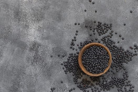 Wooden bowl of black beluga lentils beans on grey table top view. Healthy eating, protein source for vegan and vegetarian diet. Traditional Asian and North African cuisines ingredient