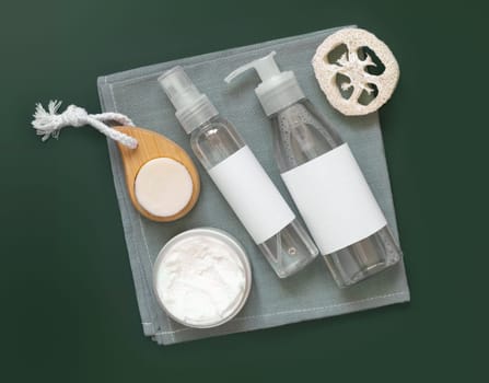 Homemade Cosmetics in plastic jars and bottles on grey towel top view on dark green. Brand packaging mockup. Organic natural cosmetics for skin and hair care